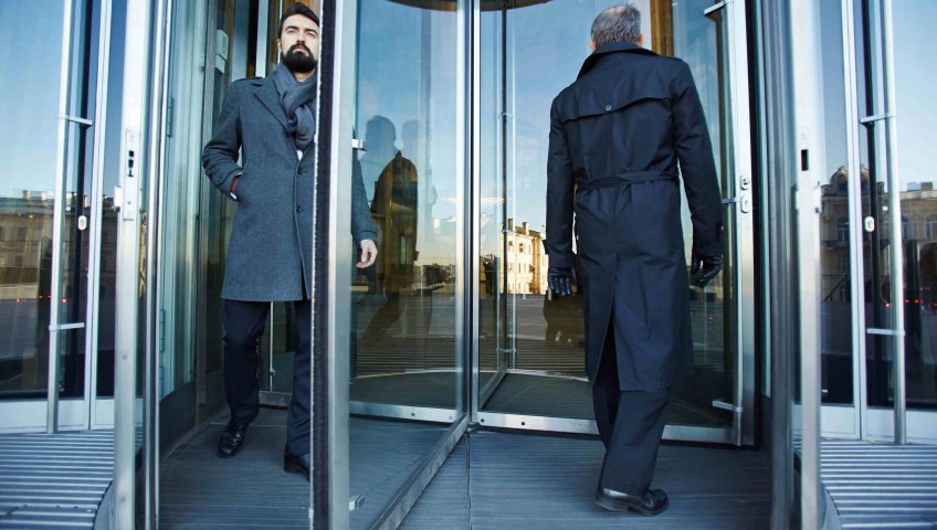 Automated solutions for commercial doors, two men walking through a revolving door.